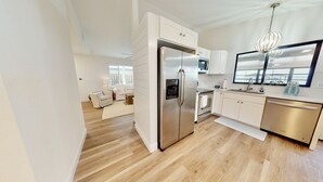 A modern kitchen with a stainless steel refrigerator, a microwave, and a dishwasher. There is a wooden floor and white cabinetry. - Relaxing Renovated Cottage on  Lake June in Winter with Dock! (Lake Placid)