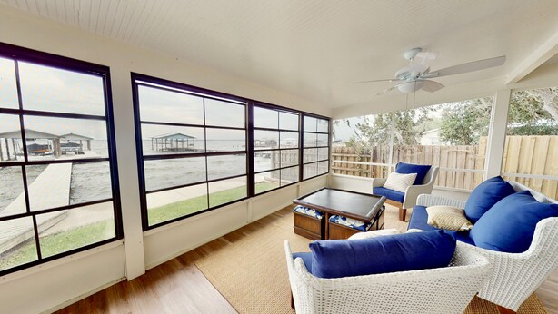 A sunroom with large windows, a ceiling fan, wicker furniture, and a view of a dock and water. - Relaxing Renovated Cottage on  Lake June in Winter with Dock! (Lake Placid)