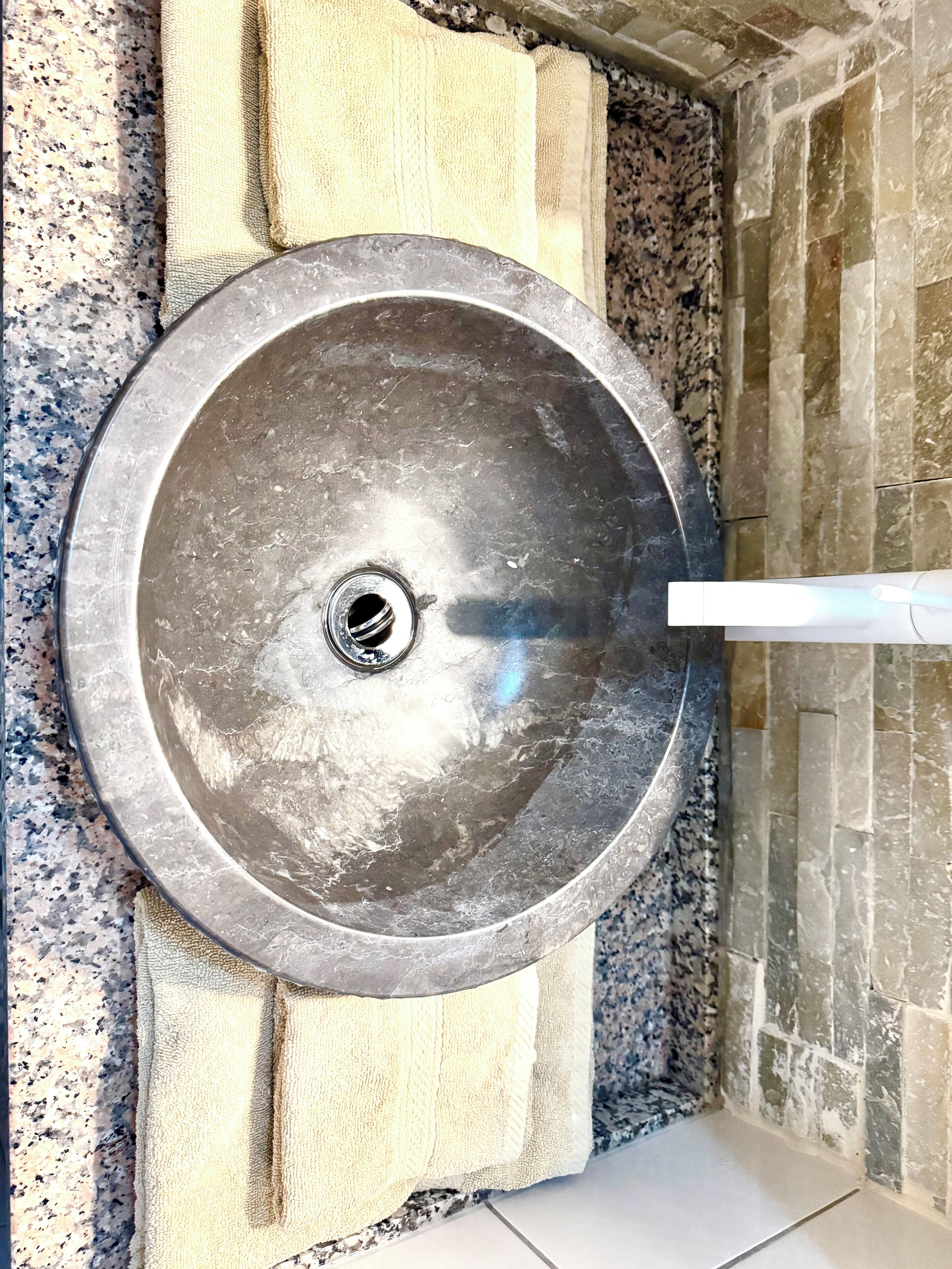 A metallic sink with a drain, mounted on a textured wall with a stone-like pattern.