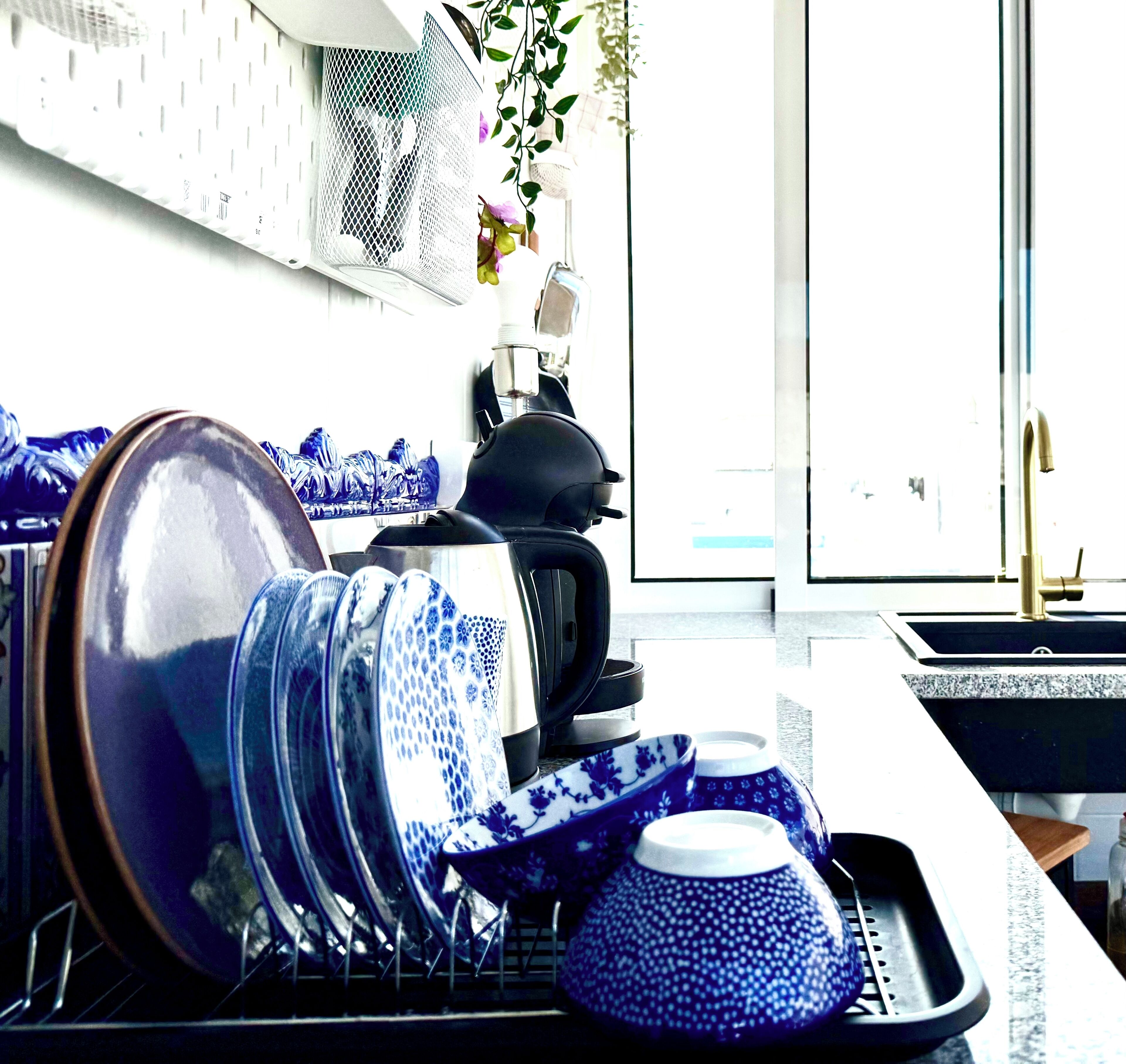 A kitchen with a dish rack full of blue and white dishes, a kettle, and a sink.