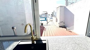 A sink with a gold faucet on a balcony with a view of buildings and a railing.