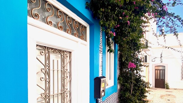 A narrow cobblestone street with a blue building featuring a decorative metal gate and a basket of flowers.