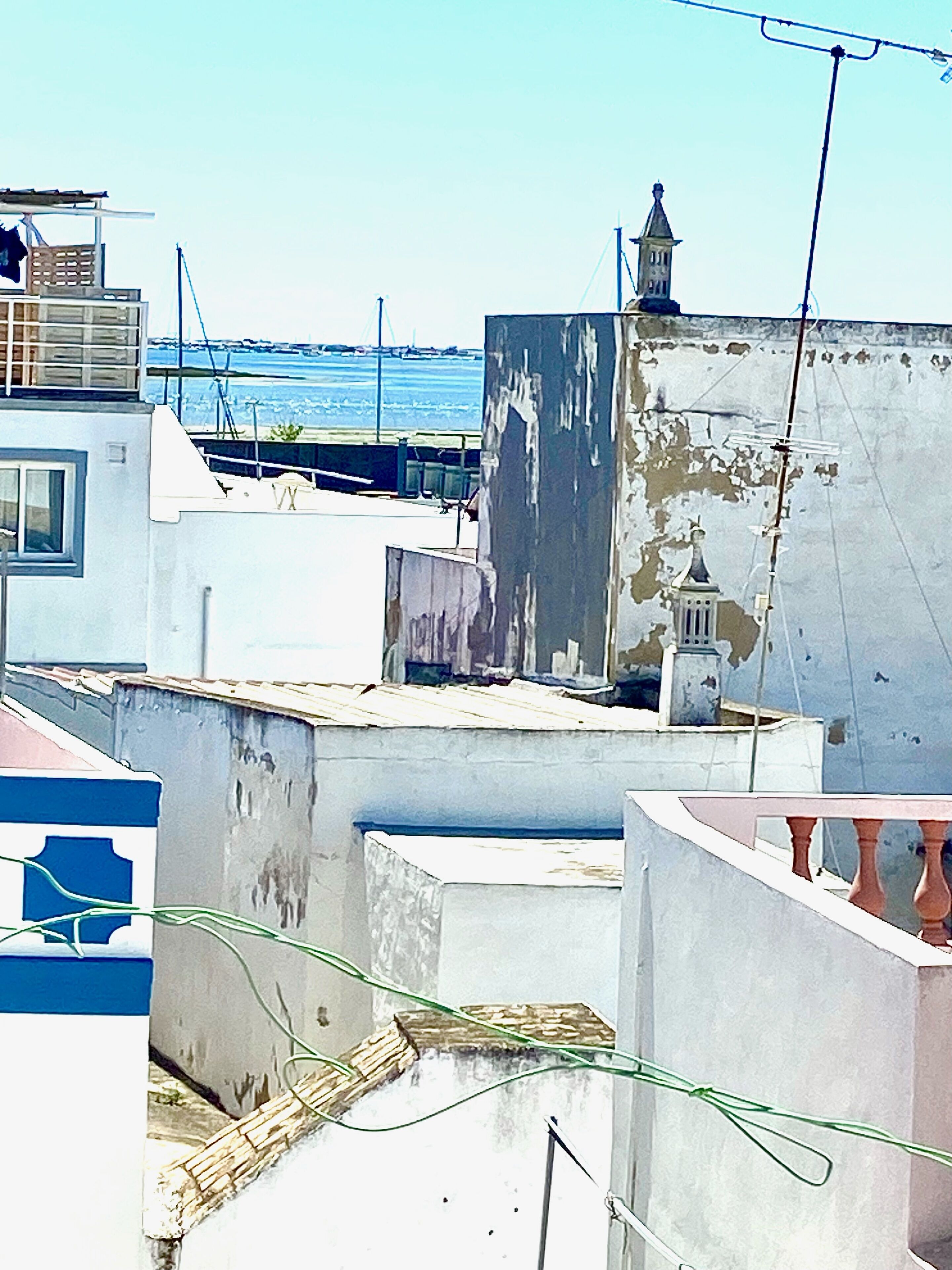 A rooftop with a view of the sea, featuring a building with a bell tower and a balcony.