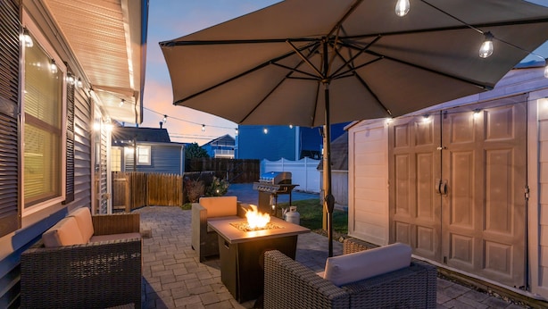 Een terras buiten met rieten meubilair, een vuurkorf en een parasol.