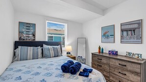 Een opgemaakt bed met opgerolde handdoeken, een bedlampje en een dressoir met decoratieve voorwerpen.