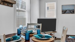 Een eetgedeelte met een tafel gedekt voor twee personen, een televisie op een standaard en een schilderij aan de muur.