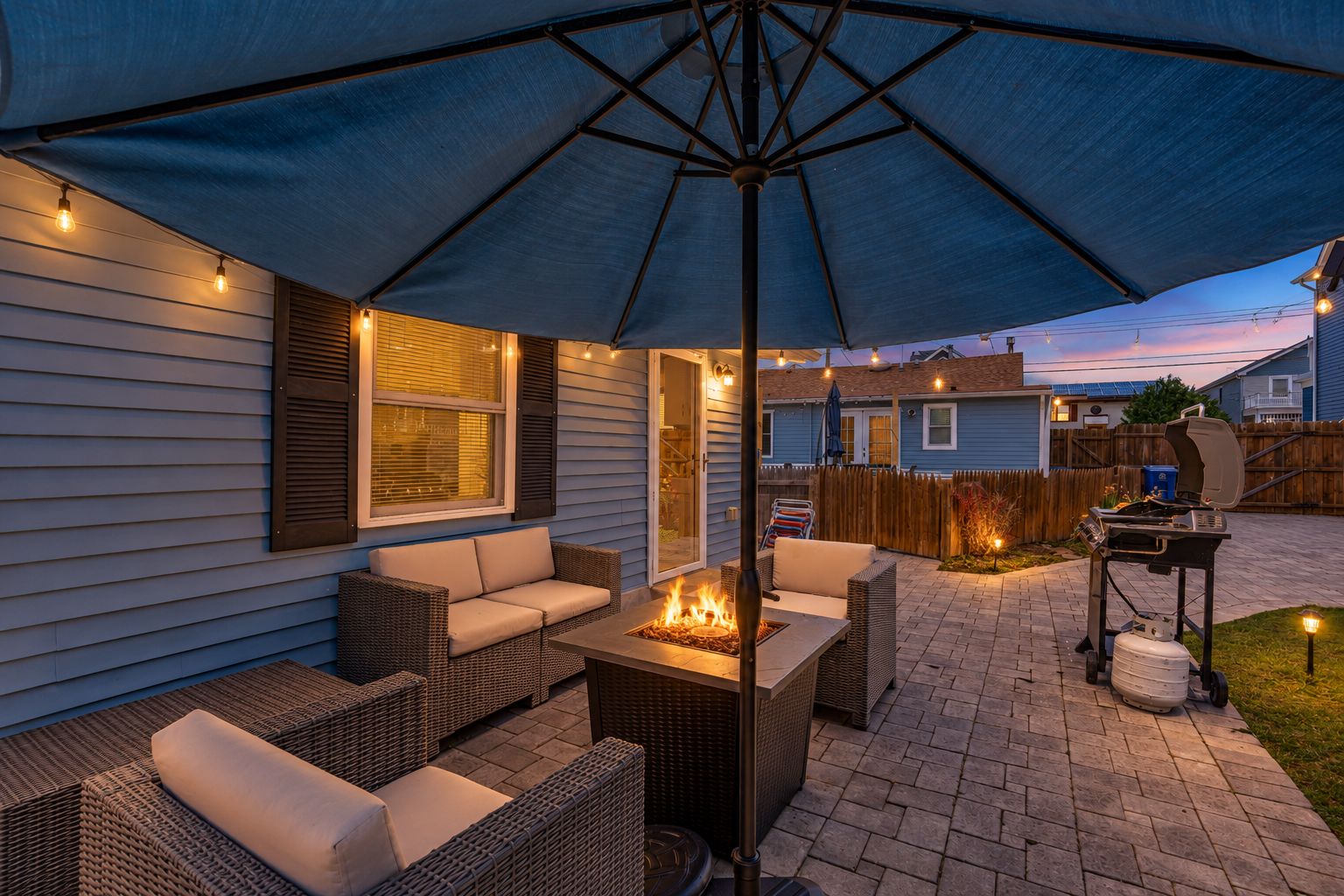An outdoor patio area with a fire pit, wicker furniture, and a large umbrella.