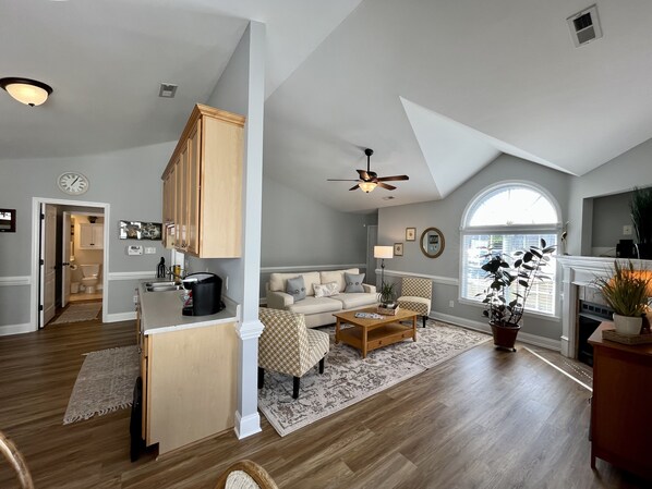 Een ruime woonkamer met een hoge plafond, een eethoek met houten kasten en een groot raam dat voor natuurlijk licht zorgt.