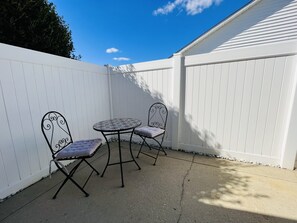 Une terrasse avec deux chaises en métal et une table, entourée d’une clôture blanche.