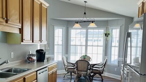 A spacious kitchen with wooden cabinets, a stainless steel dishwasher, and a dining area with a table and chairs. - New! Charming Townhome 3 Minutes to Campbell (Lillington)