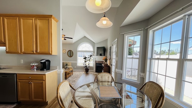 A spacious kitchen with wooden cabinets, a dining area with a glass table and wicker chairs, and large windows offering a view of the outdoors. - New! Charming Townhome 3 Minutes to Campbell (Lillington)