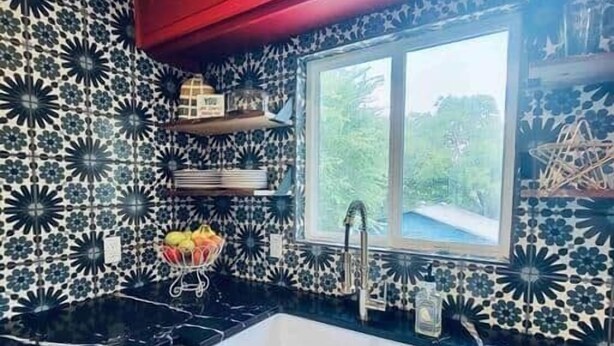 A kitchen with a black countertop, white cabinets, a window, and a patterned backsplash.