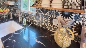 A kitchen with black marble countertops, red cabinets, and patterned tile backsplash.