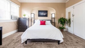 A bedroom with a bed, dresser, bedside tables, and a window.