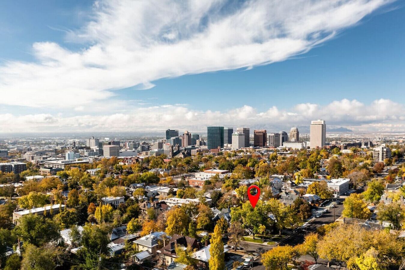 A cityscape with a mix of residential and commercial buildings, a prominent red location marker, and a clear sky.