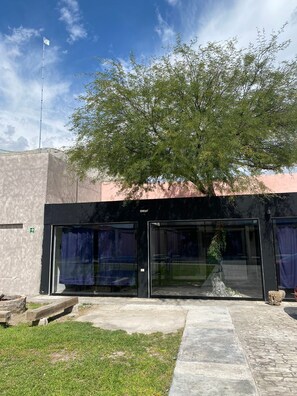 A building with a glass entrance, a tree in front, and a clear sky. - Quinta del Eden/9PX/Pool/BBQ/Pet Friendly (Matehuala)