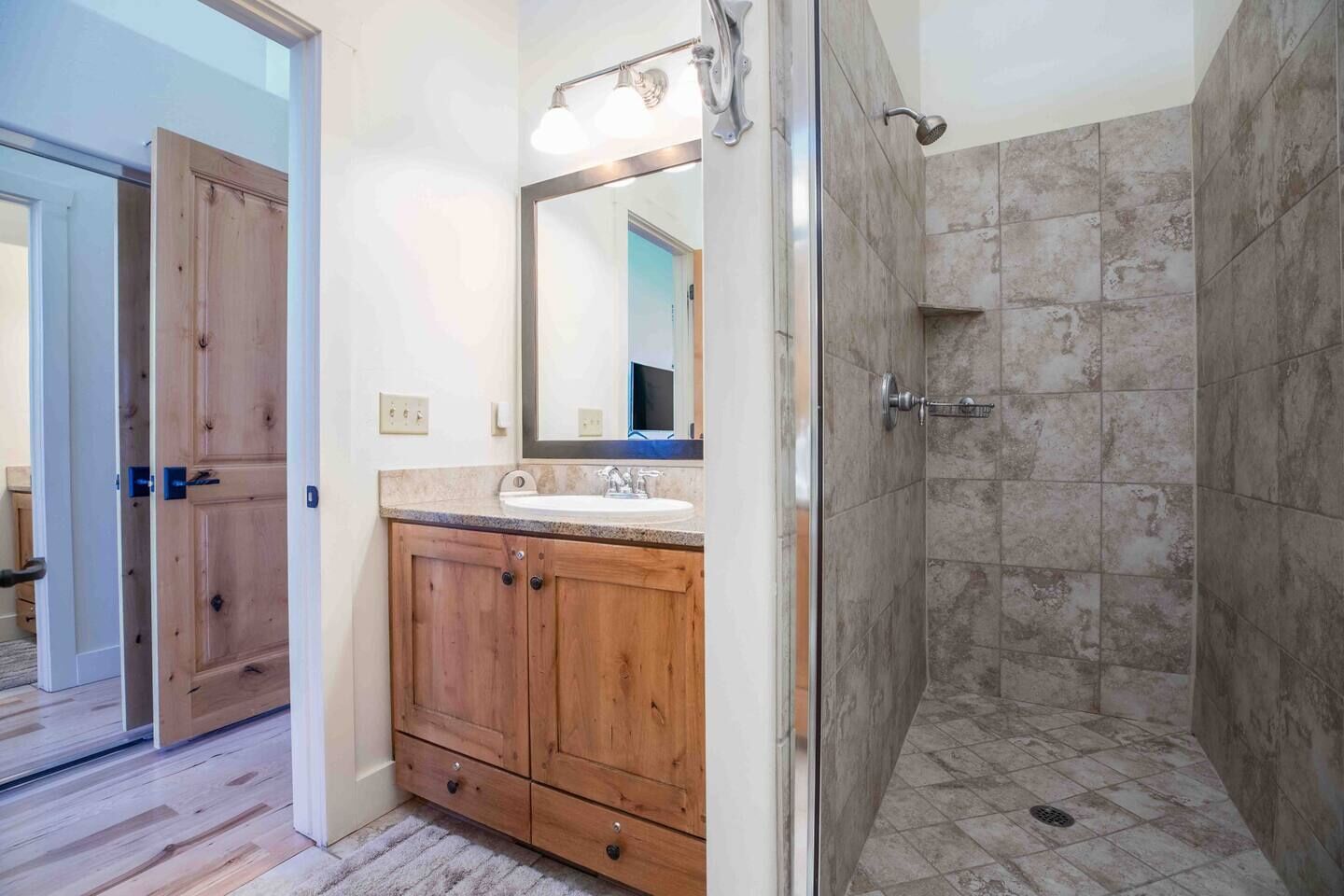 A bathroom with a wooden vanity, a sink, a mirror, and a shower area with stone tiles.