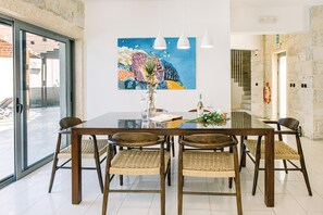 Un comedor con una mesa de vidrio, seis sillas de mimbre, un jarrón con flores y un cuadro colorido en la pared.