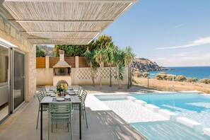An outdoor dining area with a pool, a grill, and a view of the sea.