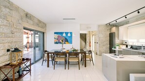 A modern kitchen with a stone wall, a dining area with a glass table, and a kitchen island. - Villa Corallium in Sfinari - 5 min from the beach (Sfinari)