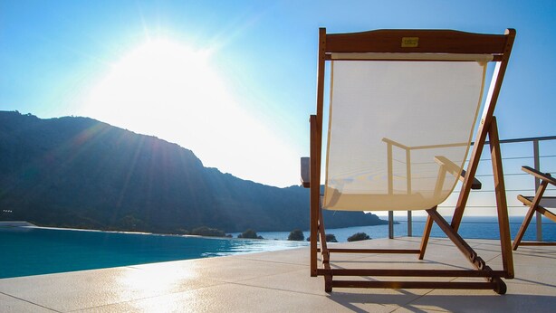 A beach chair with a mesh backrest and wooden frame, positioned on a tiled deck with a view of the ocean and mountains in the background. - Villa Corallium in Sfinari - 5 min from the beach (Sfinari)