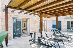 Un espacio de estar al aire libre techado, con sillones de descanso y un edificio de piedra con amplias puertas de vidrio.