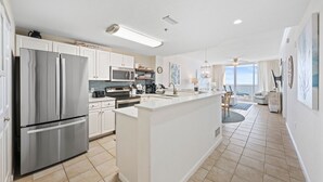 Uma cozinha moderna com eletrodomésticos de aço inoxidável, uma ilha central e vista para a sala de estar.
