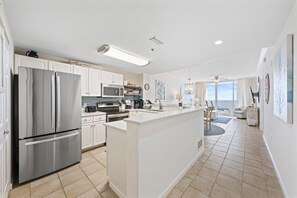 A modern kitchen with stainless steel appliances, a central island, and a view to the living area.