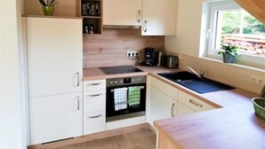 A compact kitchen with white cabinets, a built-in oven, a sink, and a window with a view of greenery outside.