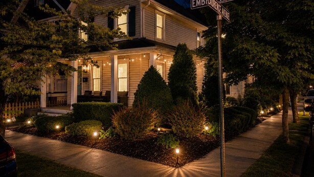 Una casa en la Avenida Embelliance con un porche, luces colgantes y un jardín bien cuidado.