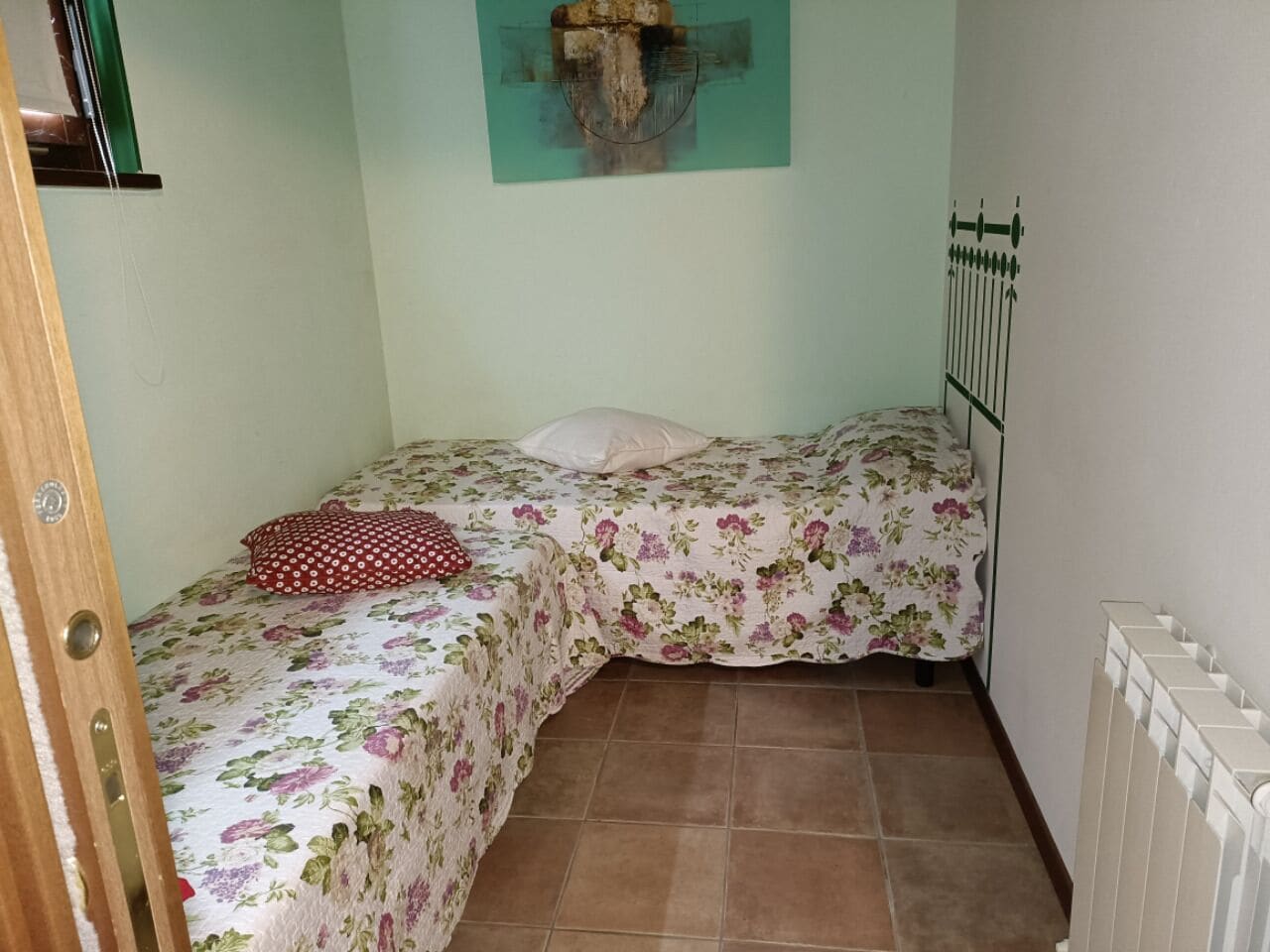 Quarto pequeno com duas camas, um radiador e uma obra de arte pendurada na parede.