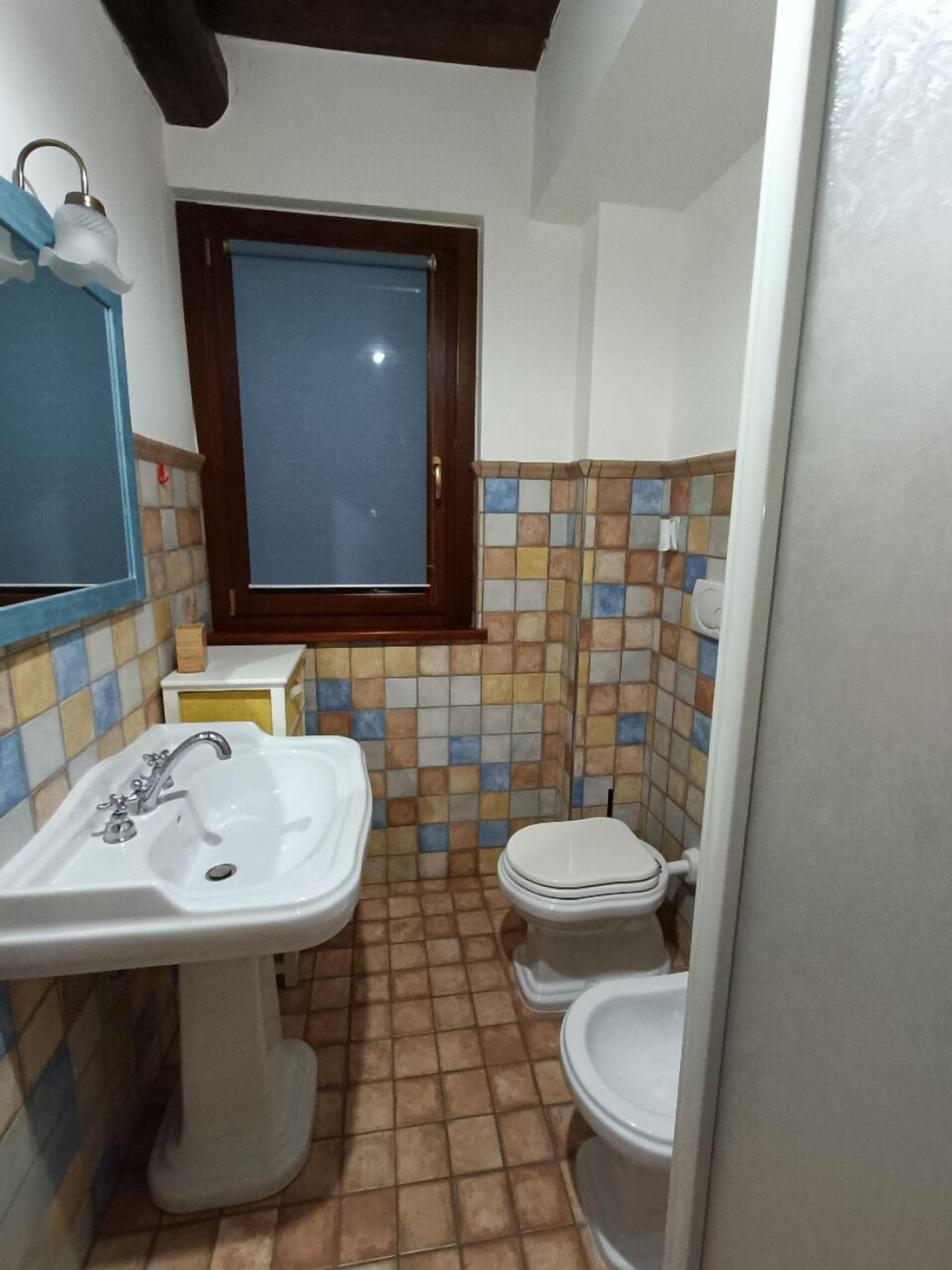 Un baño con un lavamanos blanco, un inodoro y una ventana con marco de madera.