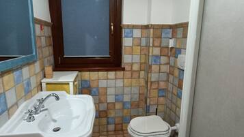 Un baño con un lavamanos blanco, un inodoro y una ventana con marco de madera.