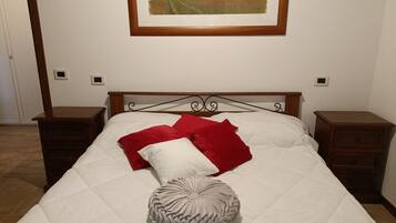 Ein Schlafzimmer mit einem Bett, zwei Nachttischen, einem hölzernen Kopfteil und einem gerahmten Landschaftsbild über dem Bett.