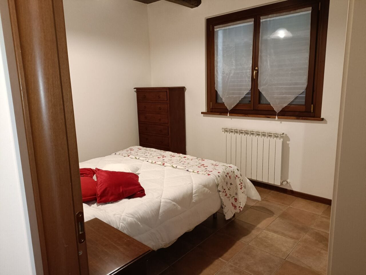 A bedroom with a bed, a wooden wardrobe, a radiator, and a window with a curtain.