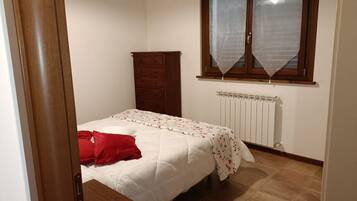 A bedroom with a bed, a wooden wardrobe, a radiator, and a window with a curtain.