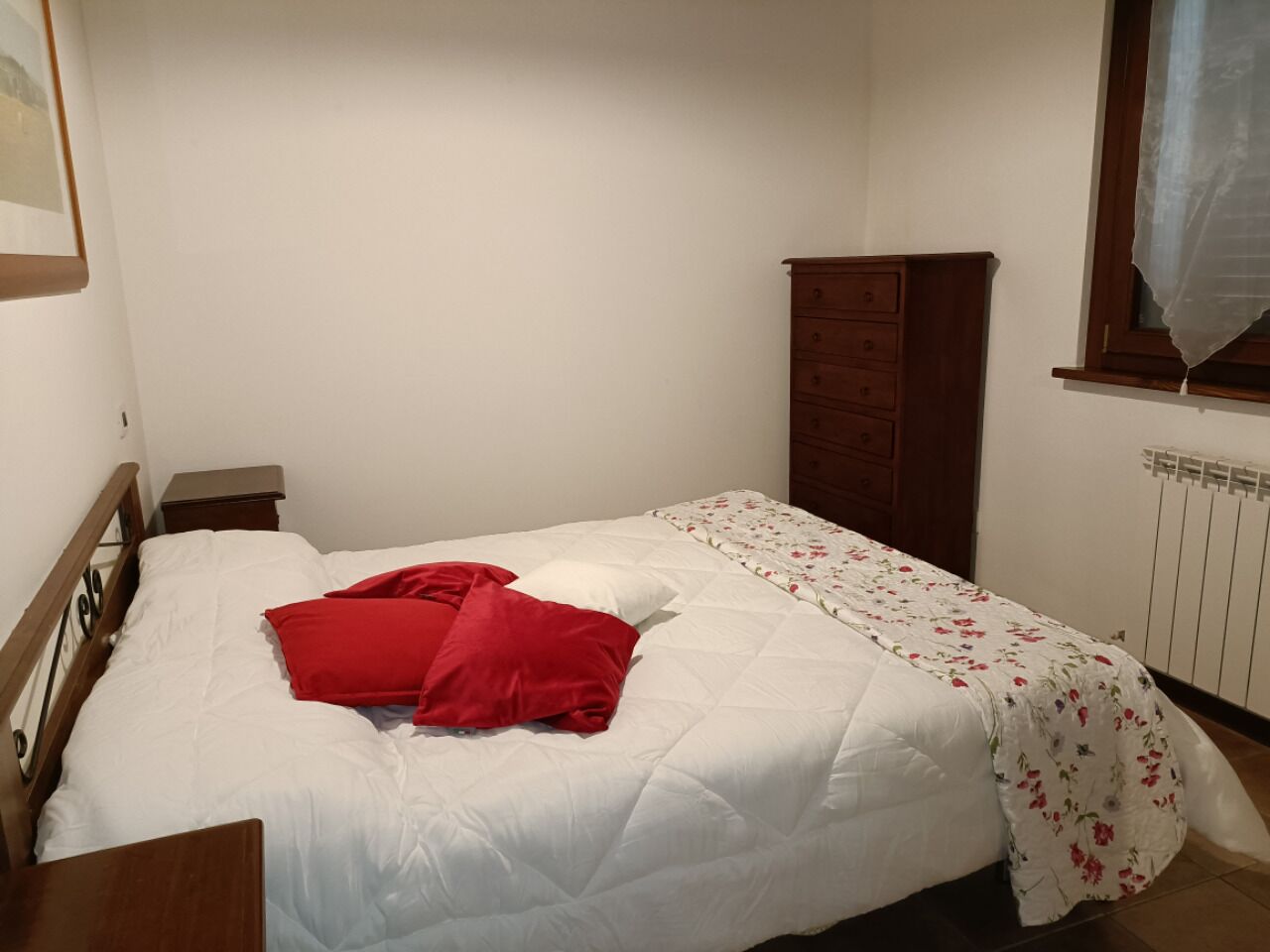 Un dormitorio con una cama individual, cabecera de madera, mesita de noche, cómoda y una ventana con cortina.