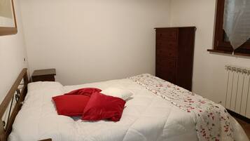 Un dormitorio con una cama individual, cabecera de madera, mesita de noche, cómoda y una ventana con cortina.