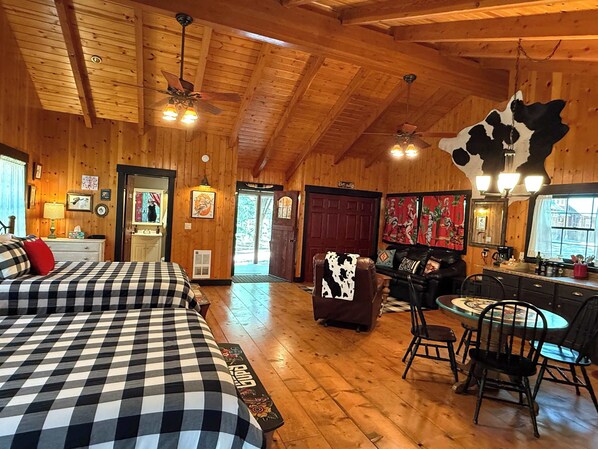 A cozy log cabin interior with a checkered bed, a dining area with a round table and chairs, and a ceiling fan.