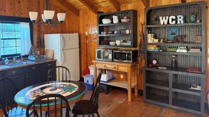 Eine gemütliche Küche mit Holzwänden und -decke, ausgestattet mit einem Kühlschrank, einer Mikrowelle und einem Holzessttisch mit Stühlen.