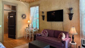 Una sala de estar acogedora con un sofá morado, una mesita, un televisor montado en la pared y una puerta que dice 'Powder Room'.