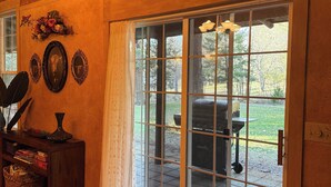 A room with a sliding glass door leading to an outdoor patio, a wooden console table with decorative items, and a patterned rug. - Cedar House • King Suite • Soaking Tub • WiFi • A/C (Selma)