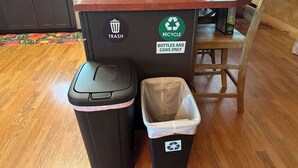 A trash bin and recycling bin in a kitchen area with a wooden table and chairs. - Cedar House • King Suite • Soaking Tub • WiFi • A/C (Selma)