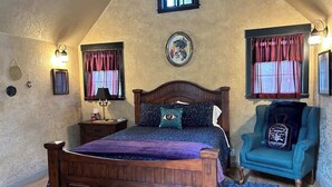 Quarto com cama de madeira, mesa de cabeceira, cadeira e luminária fixada na parede.