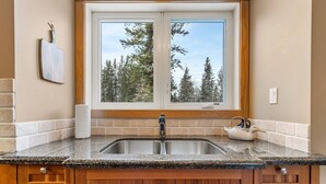 Una cocina con un lavamanos doble, armarios de madera y un ventanal con vistas a árboles.