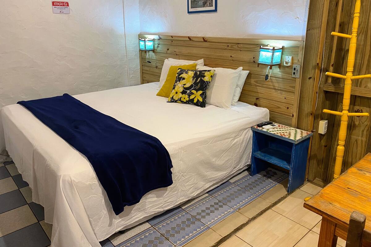 A neatly made bed with white linens and a blue blanket, flanked by two wall-mounted lamps.