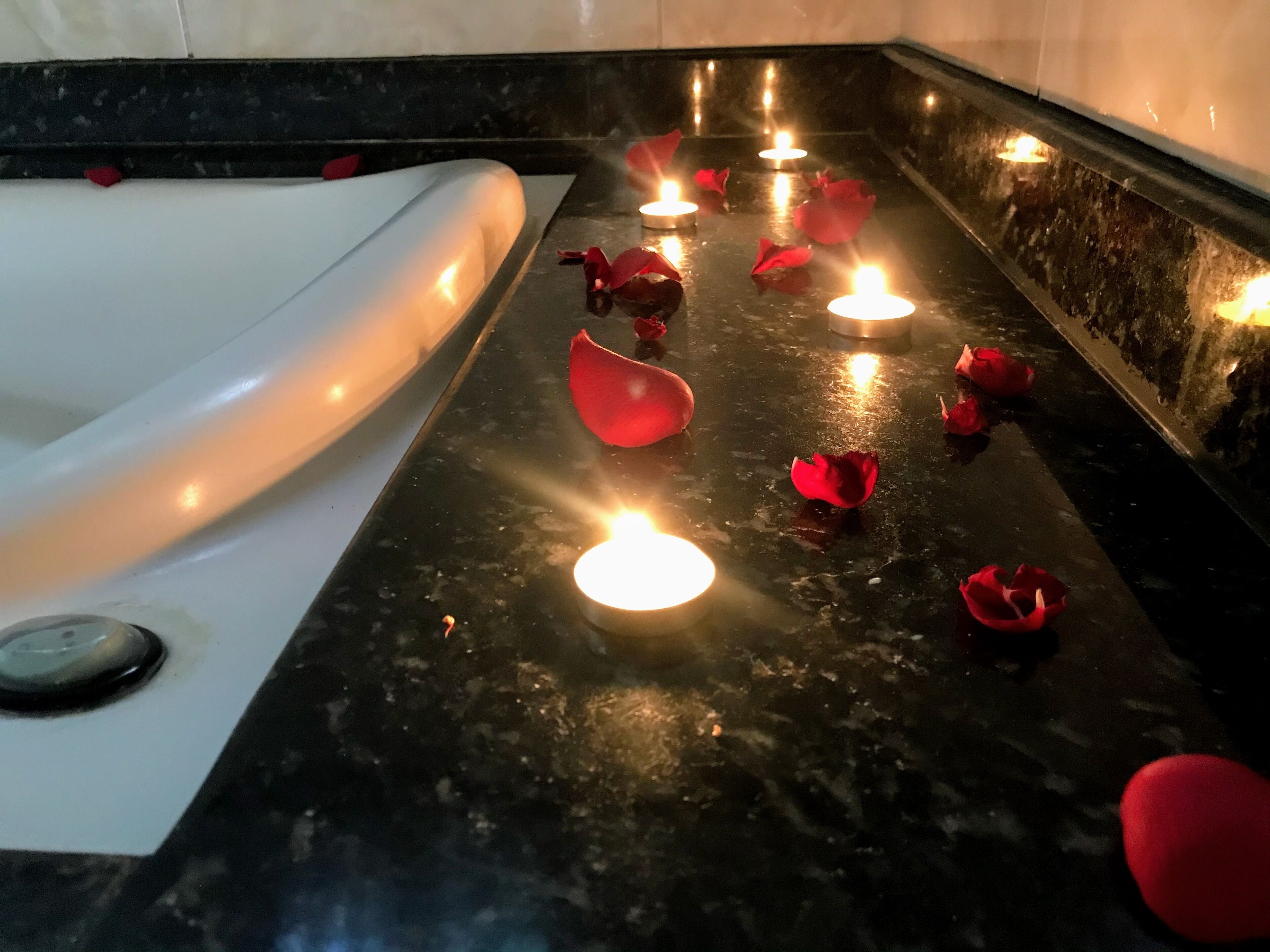 Una bañera con velas y pétalos de rosa sobre un revestimiento de mármol oscuro.