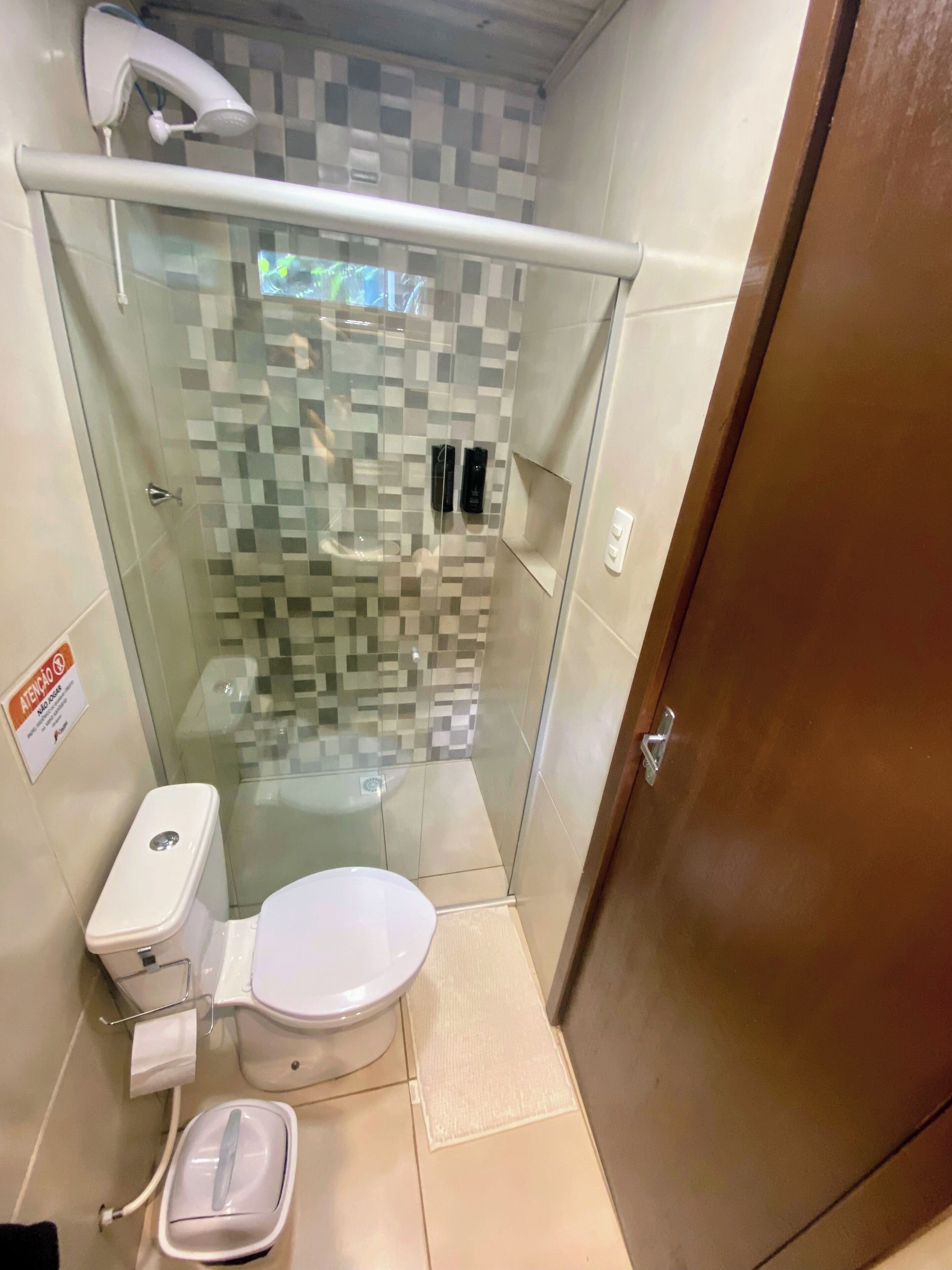 Un baño pequeño y cerrado con cabina de ducha de vidrio, inodoro y secador de manos.