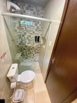 Un baño pequeño y cerrado con cabina de ducha de vidrio, inodoro y secador de manos.