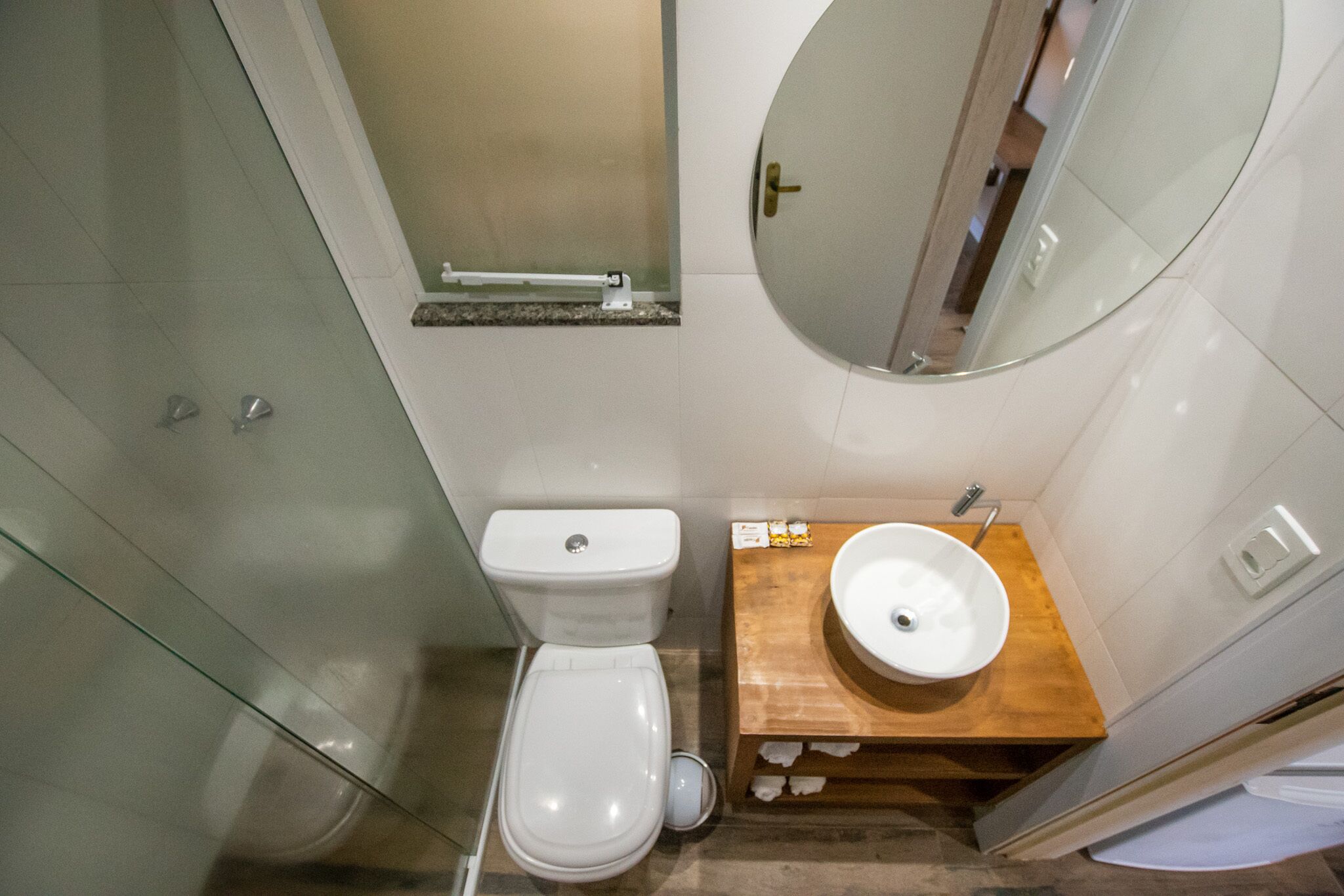 Un baño compacto con cabina de ducha de vidrio, inodoro blanco y tocador de madera con lavamanos.